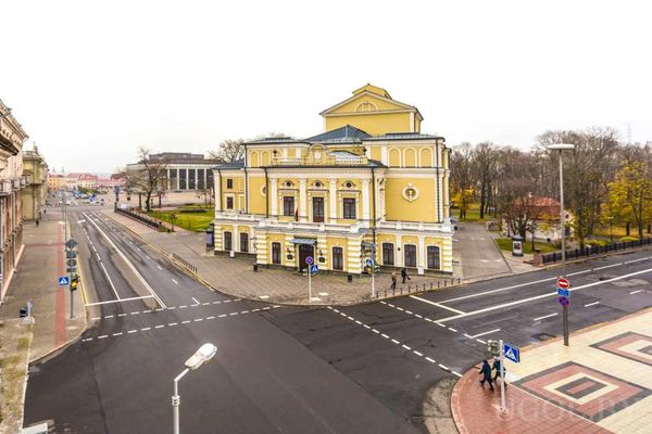 Городской перекрёсток с жёлтым классическим зданием, тротуарами и фонарями.