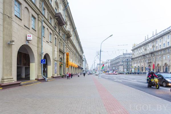 Городская улица с арочными фасадами, жёлтыми навесами, пешеходами и машинами.