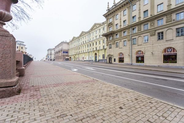 Широкая пустая улица с классическими зданиями, арочными входами и брусчатым тротуаром.