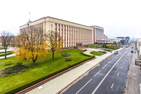 Большое административное здание с симметричным фасадом, флагом на крыше и ухоженным газоном.